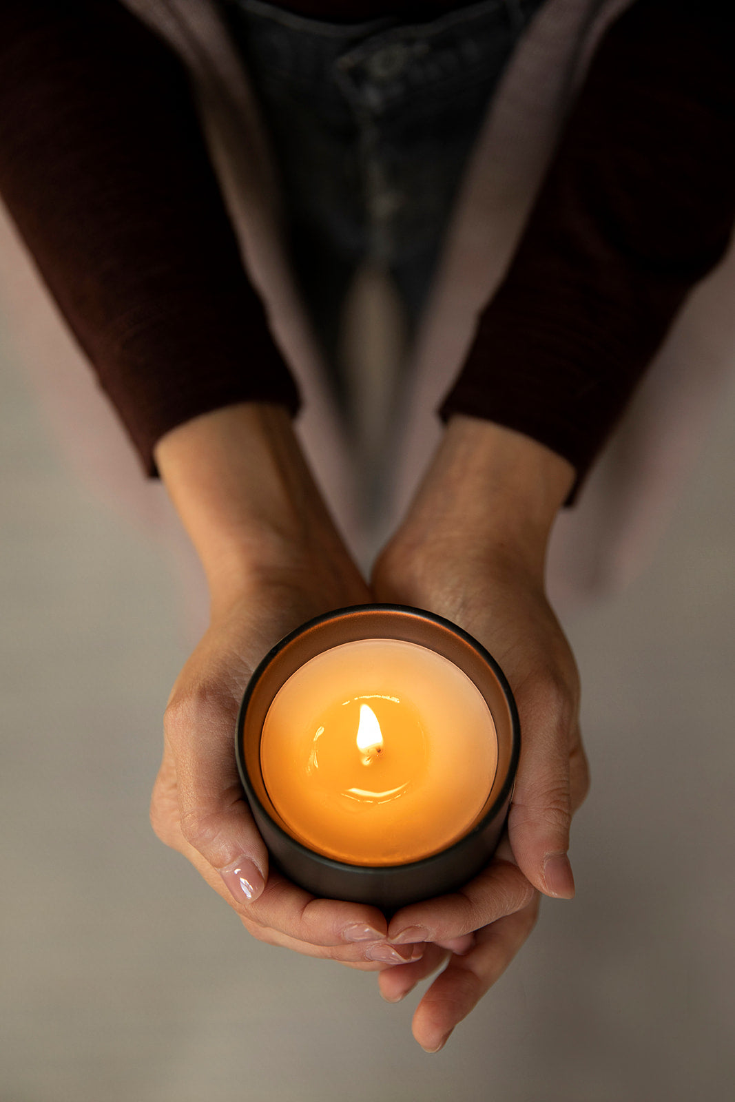 Aerial shot of hands gently holding the burning Vellie Hope Candle, creating a peaceful, serene atmosphere with uplifting fragrance notes of bergamot, lemon, ylang ylang, and rose. Wax is coconut and soy.