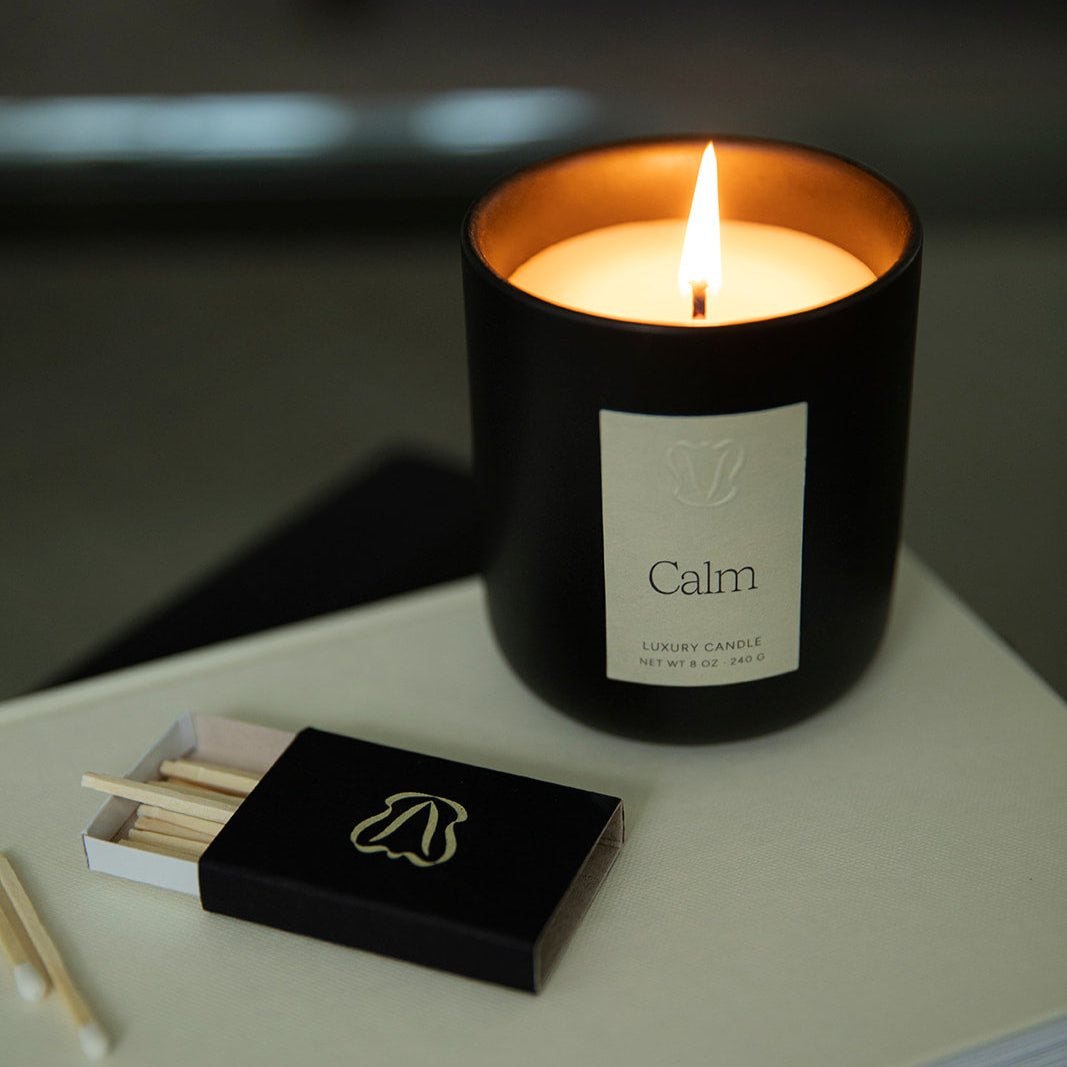 Vellie Calm Candle burning on top of a book in the living room, offering grounding sandalwood and vetiver scents amongst other notes.