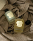 Two wrap sprays scents Open and Calm delicately placed on top of a Vellie Wrap. Created to spray on your wrap. The image is a fragrant reminder of love, making each wrap feel like a personal sanctuary.