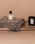 All My Love Gift Bundle flatlay. Wooden board showcases the products in the set. An oat baby alpaca wrap, a luxury candle in the scent Calm and an all natural wrap spray. All pieces are by Vellie.