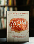 Mom Enough book by Rachel Martin, displayed in a cozy indoor library highlighting the book as a beautiful addition to any home. This book is a gift of love, encouragement, and support for mothers.