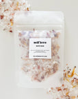 Self Love bath soak by The Bohemian Box Shop. Made in USA all natural ingredients: sea salt, Himalayan salt, rose, petals, calendula petals and pure essential oil blend. Salts are transparent color and light pink with yellow calendula petals.