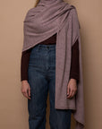 Mauve Vellie wrap draped over one shoulder, made from hypoallergenic, antimicrobial baby alpaca fiber—luxurious, durable, and low-maintenance. Color is soft Mauve, almost lavender.