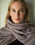 Model looking directly into the camera, wearing the mauve Vellie wrap styled as a scarf. Crafted from hypoallergenic, antimicrobial baby alpaca fiber, offering luxurious warmth.