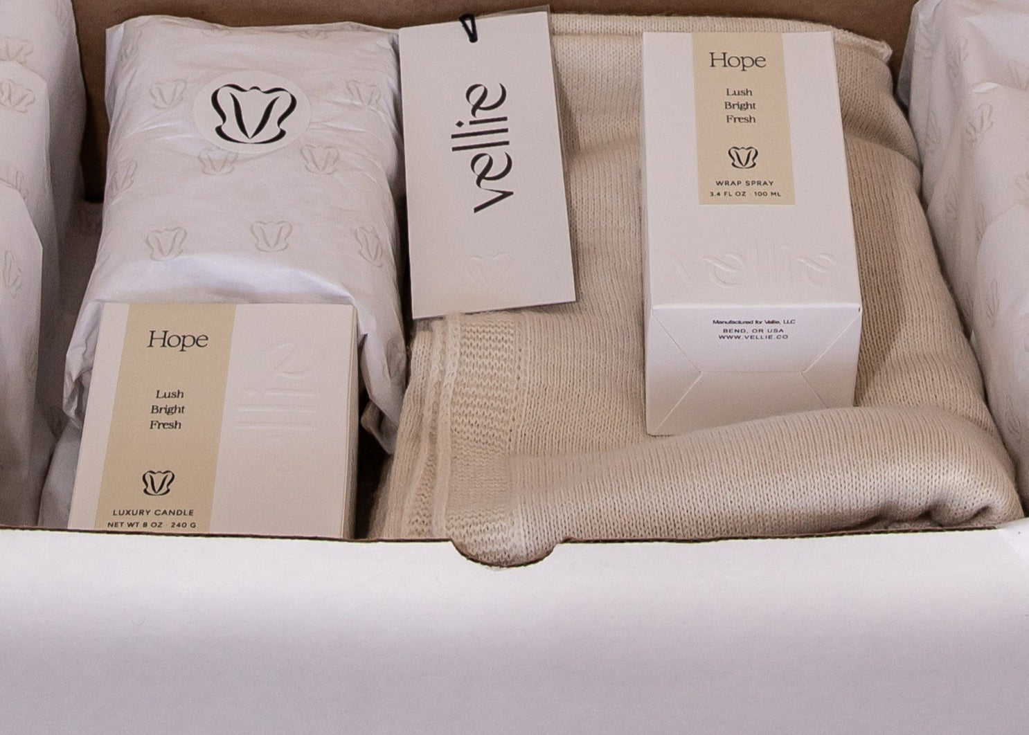 Unboxing of gift bundle. White tissue paper with cream branding V for Vellie in black. In here, an ivory baby alpaca wrap, Hope wrap spray and Hope luxury candle. Sustainable packaging inspiration.