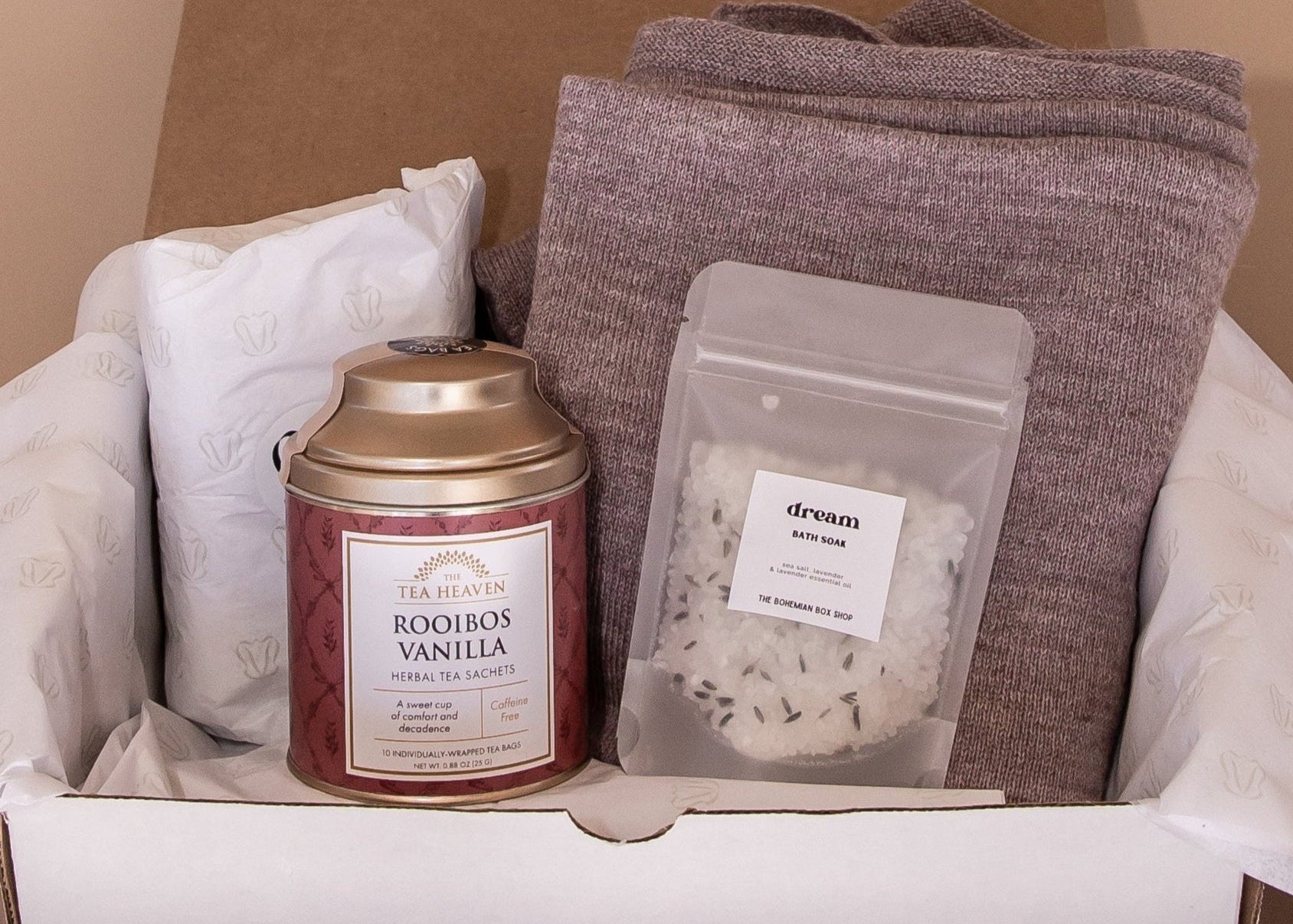 Unboxing of gift set. Inside, a canister of Rooibos Vanilla tea, 40z of bath salts by The Bohemian Box Shop and the mauve Vellie Wrap.
