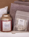 Unboxing of gift set. Inside, a canister of Rooibos Vanilla tea, 40z of bath salts by The Bohemian Box Shop and the mauve Vellie Wrap.