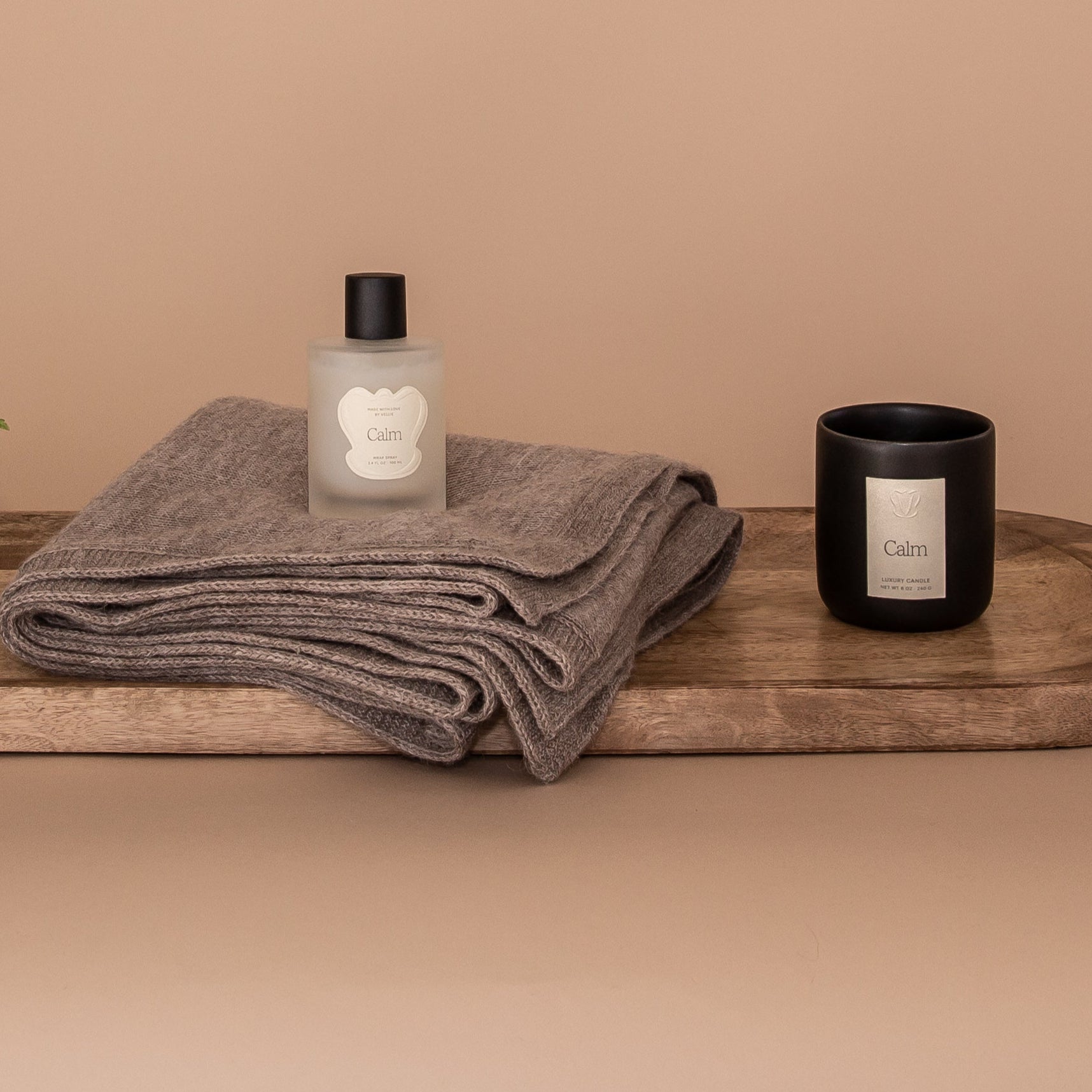 All My Love Gift Bundle flatlay. Wooden board showcases the products in the set. An oat baby alpaca wrap, a luxury candle in the scent Calm and an all natural wrap spray. All pieces are by Vellie.