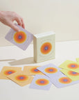 Card deck with colorful circular designs on cards and packaging, on a light surface.