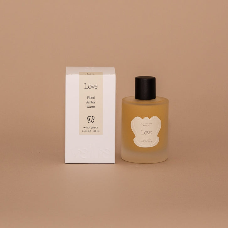 Vellie Love Wrap Spray with all-natural, clean beauty ingredients like lemon, rose, and vanilla oils, designed to enhance the scent and feel of your Vellie baby alpaca wrap. Seen here next its minimal neutral packaged box.