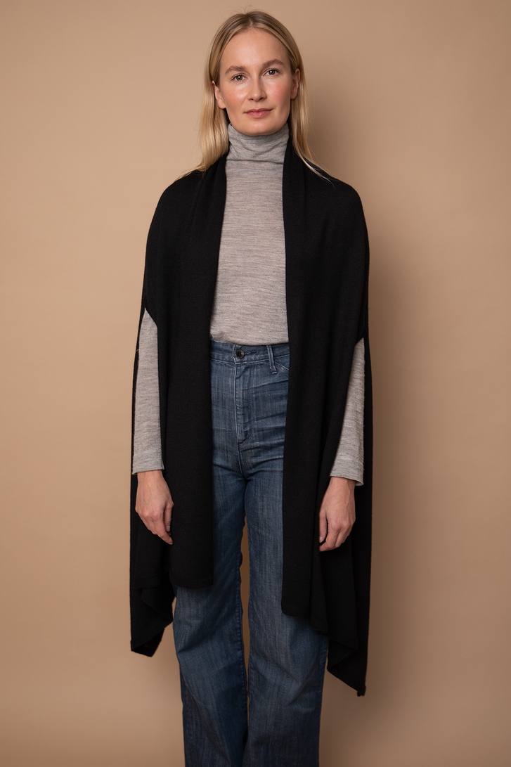 Model wearing black Vellie Wrap in a versatile open style, made from 100% fair-trade baby alpaca fiber, offering exceptional softness and warmth.