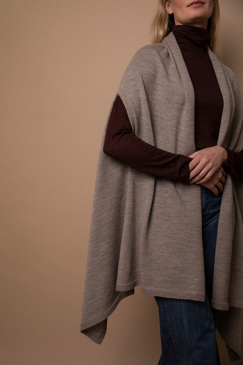 Close-up of oat Vellie wrap in movement, showcasing its beautiful drapery and luxurious texture, crafted from soft, sustainable baby alpaca fiber. Ethically made in Peru.